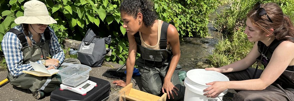 Three students wearing waders surrounded by science equipment.